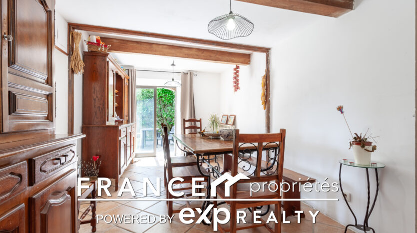 Salle à manger avec poutres et porte-fenêtre sur le jardin.